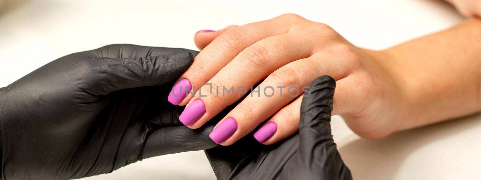 A manicurist holds beautiful young female hands showing finished purple, pink polish manicure in a nail salon