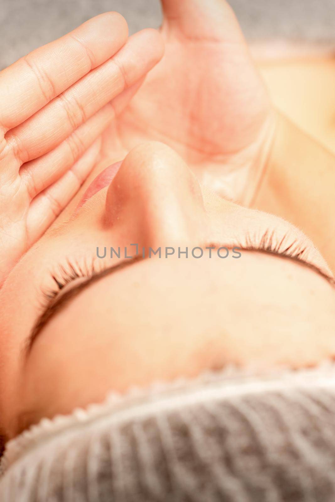 Beautiful caucasian young woman receiving a facial massage with closed eyes in spa salon, close up. Relaxing treatment concept. by okskukuruza