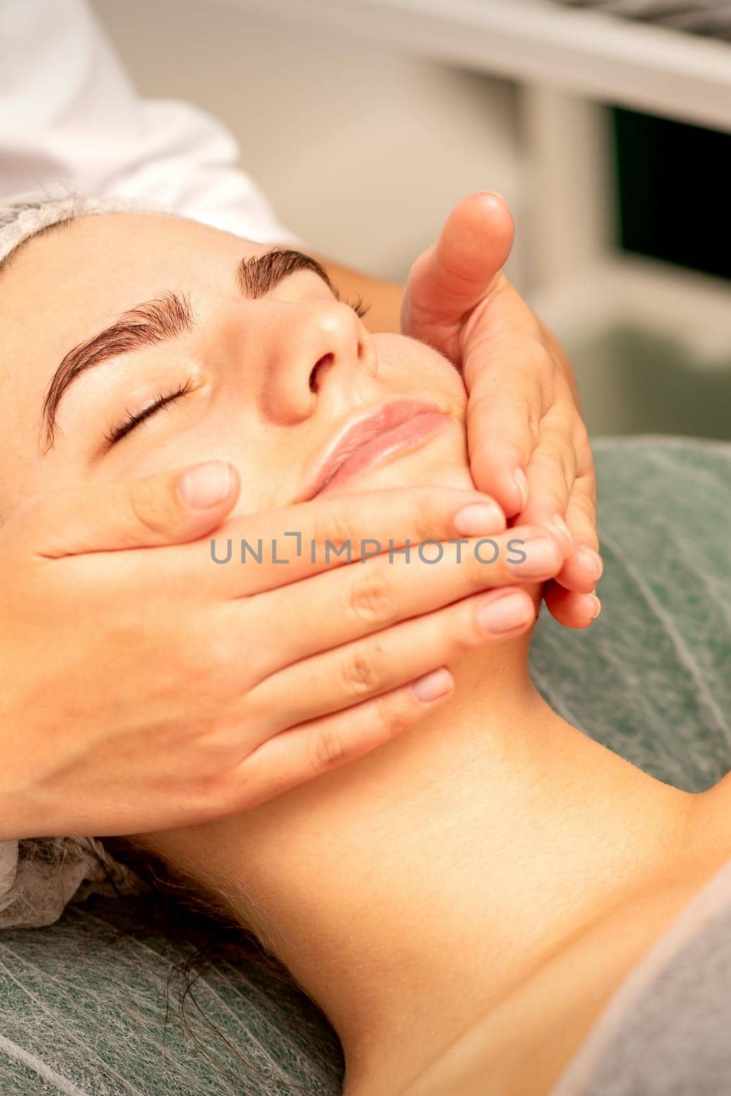 Beautiful caucasian young woman receiving a facial massage with closed eyes in spa salon, close up. Relaxing treatment concept