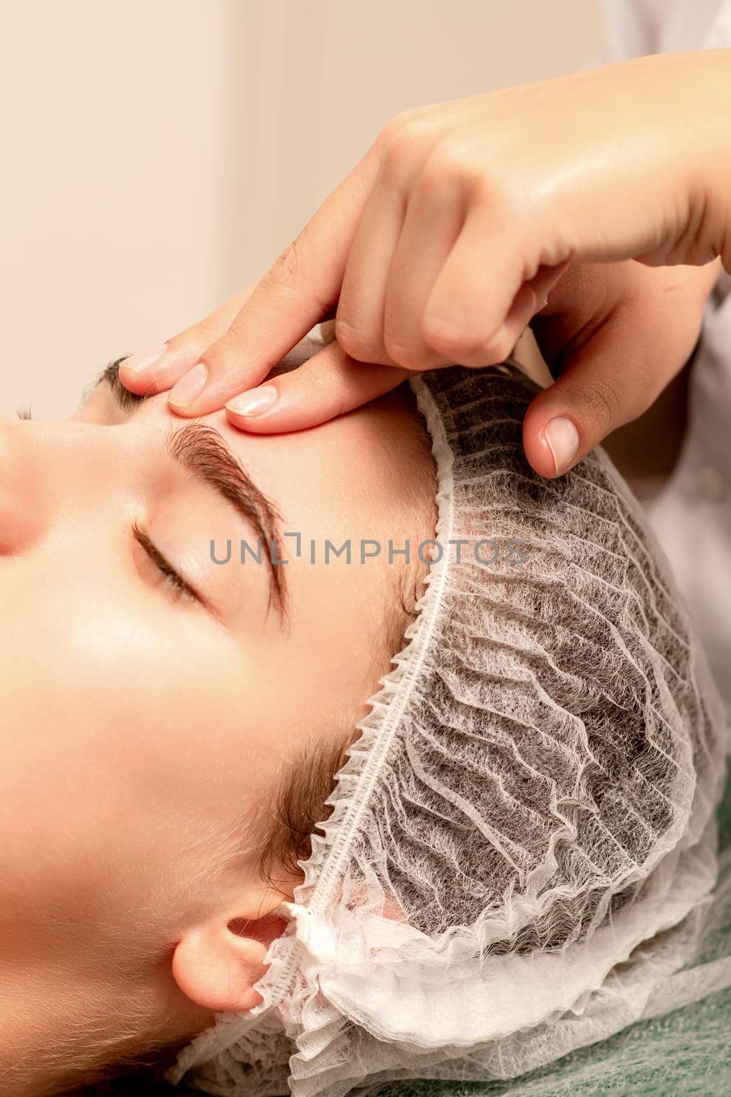 Beautiful caucasian young woman receiving a facial massage with closed eyes in spa salon, close up. Relaxing treatment concept