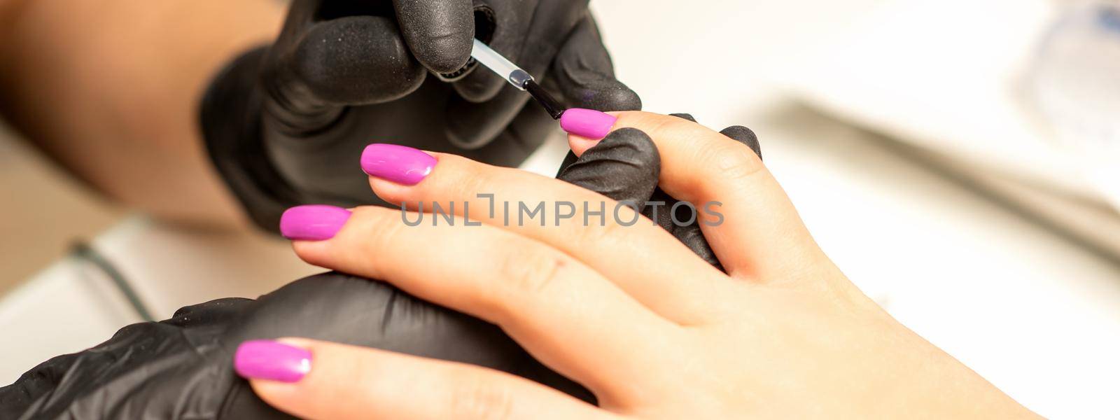 Professional manicure. A manicurist is painting the female nails of a client with purple nail polish in a beauty salon, close up. Beauty industry concept