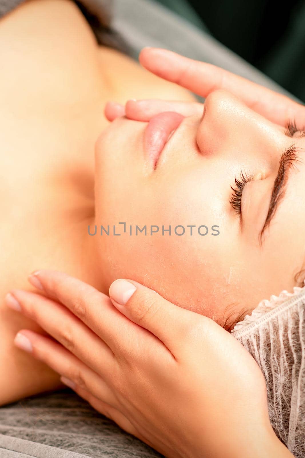 Face massage. Beautiful caucasian young white woman having a facial massage with closed eyes in a spa salon. by okskukuruza