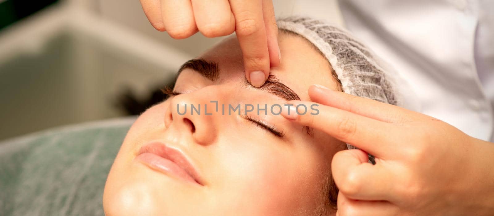 Eyebrow massage. Beautiful caucasian young white woman receiving an eye and eyebrow massage with closed eyes in a spa salon. by okskukuruza