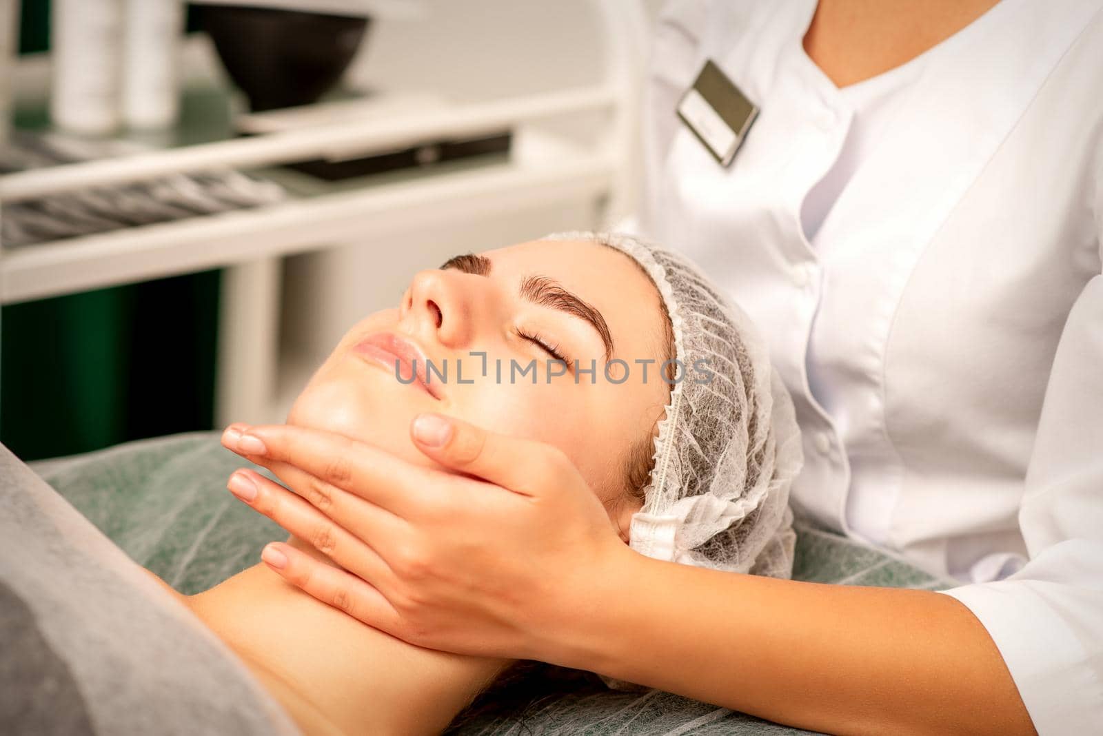 Facial massage. Hands of a masseur massaging neck of a young caucasian woman in a spa salon, the concept of health massage