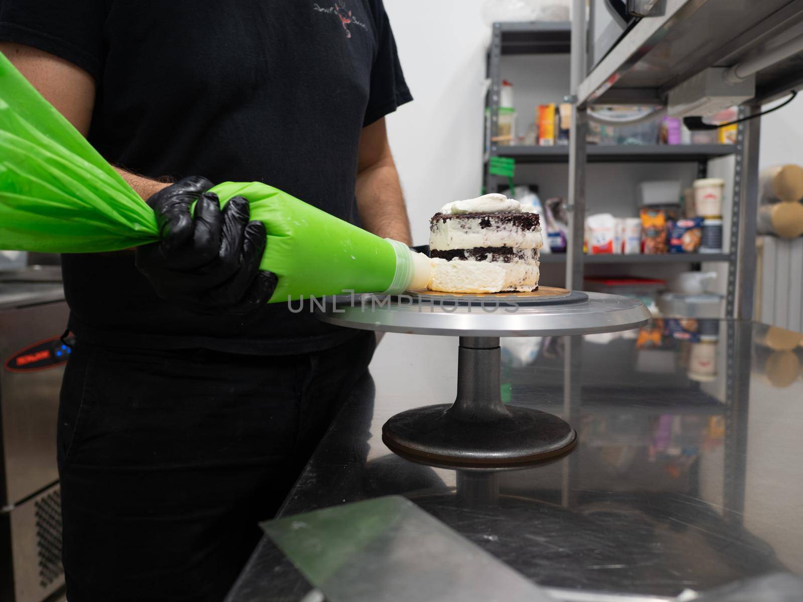 decorator applying buttercream to frosted cake with bag full of cream