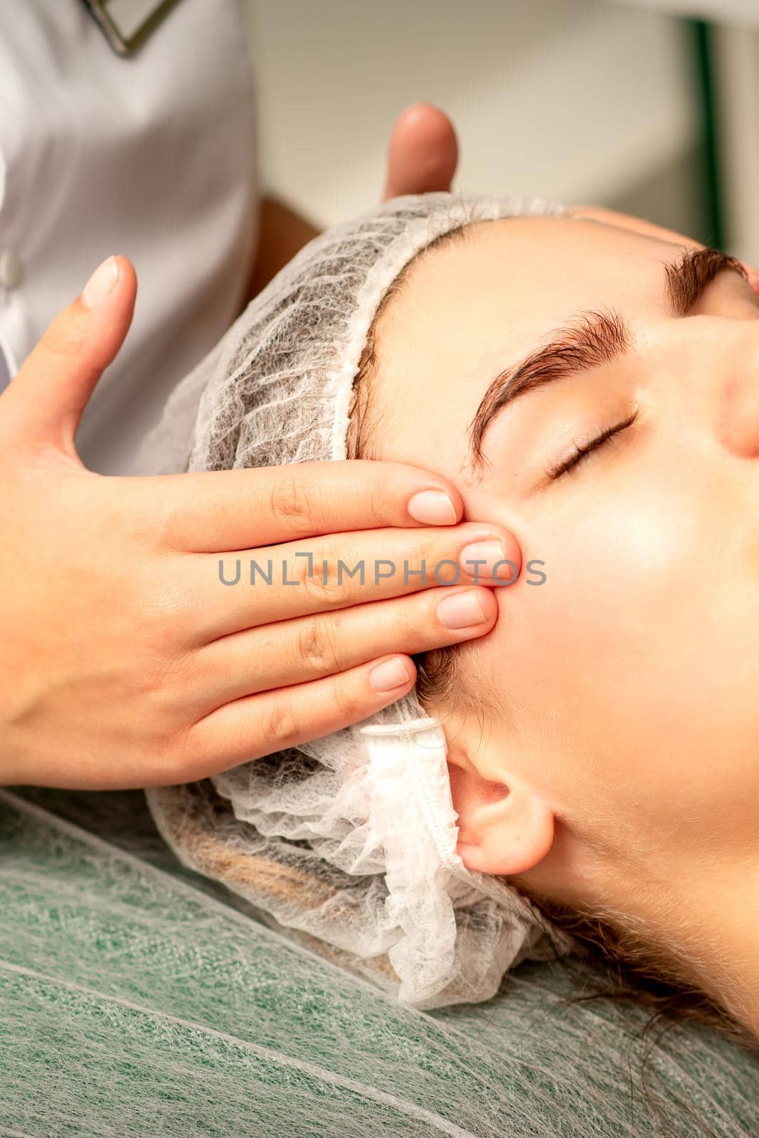 Head massage. Beautiful caucasian young white woman receiving a head and forehead massage with closed eyes in a spa salon. by okskukuruza