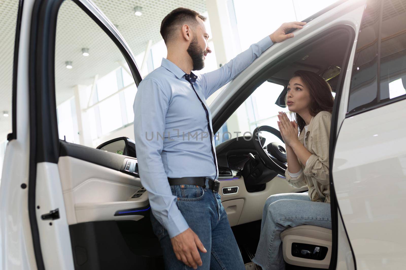 a young woman asks her husband to buy a new car at a car dealership.