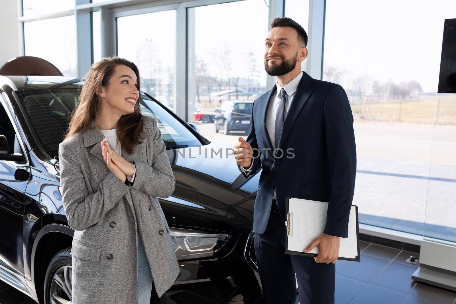 a woman buyer asks for a discount on a new car from an employee of the car showroom of the dealership.