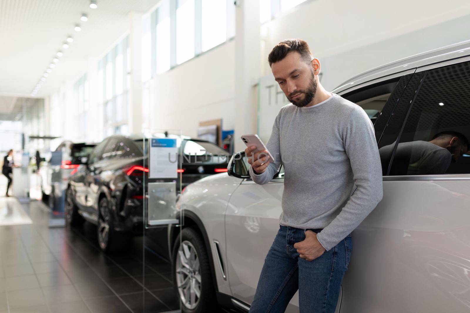 a man studies the offer of insurance companies in a car dealership on a smartphone.