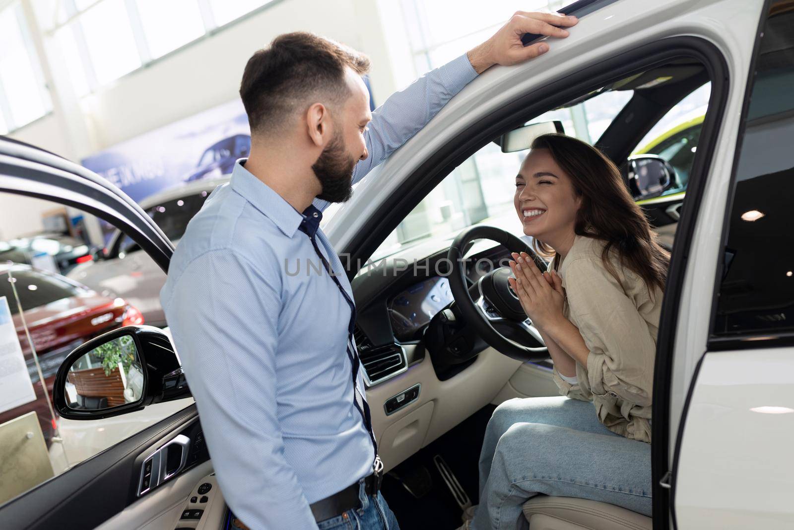 a young woman begs her husband to buy a new car at a car dealership.