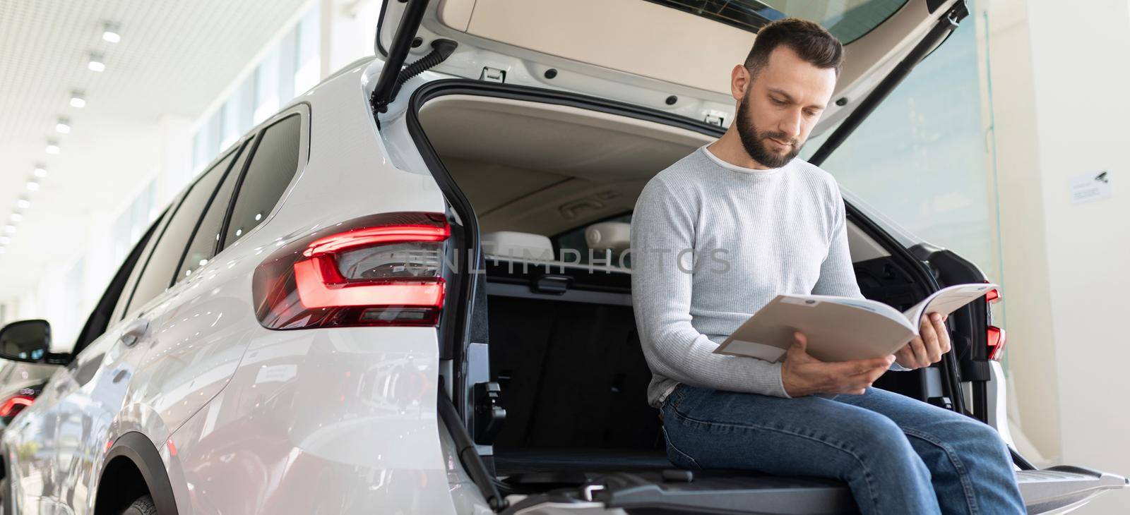 A man sits in the trunk of a car looking at an insurance offer.