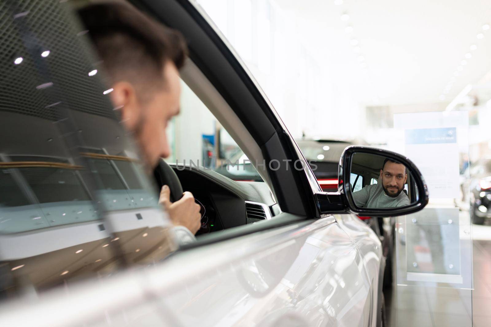a man at a car dealership driving a car looks in the rearview mirror.
