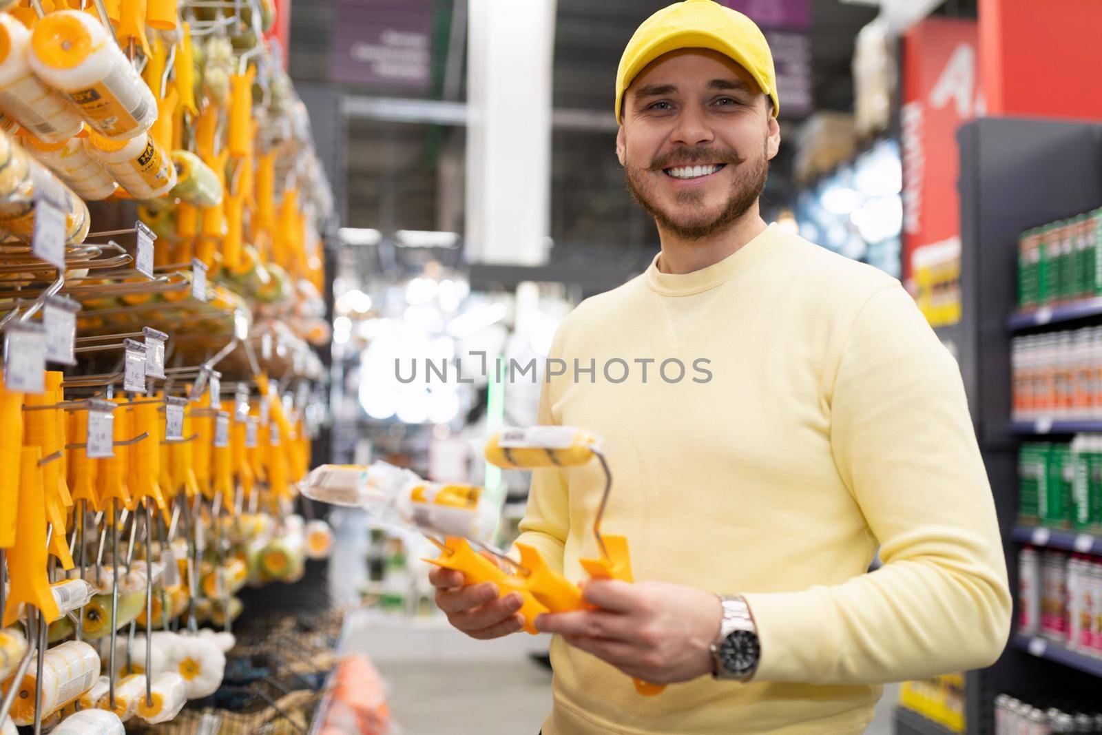 a man in a hardware store picks up a roller and brushes for painting work.