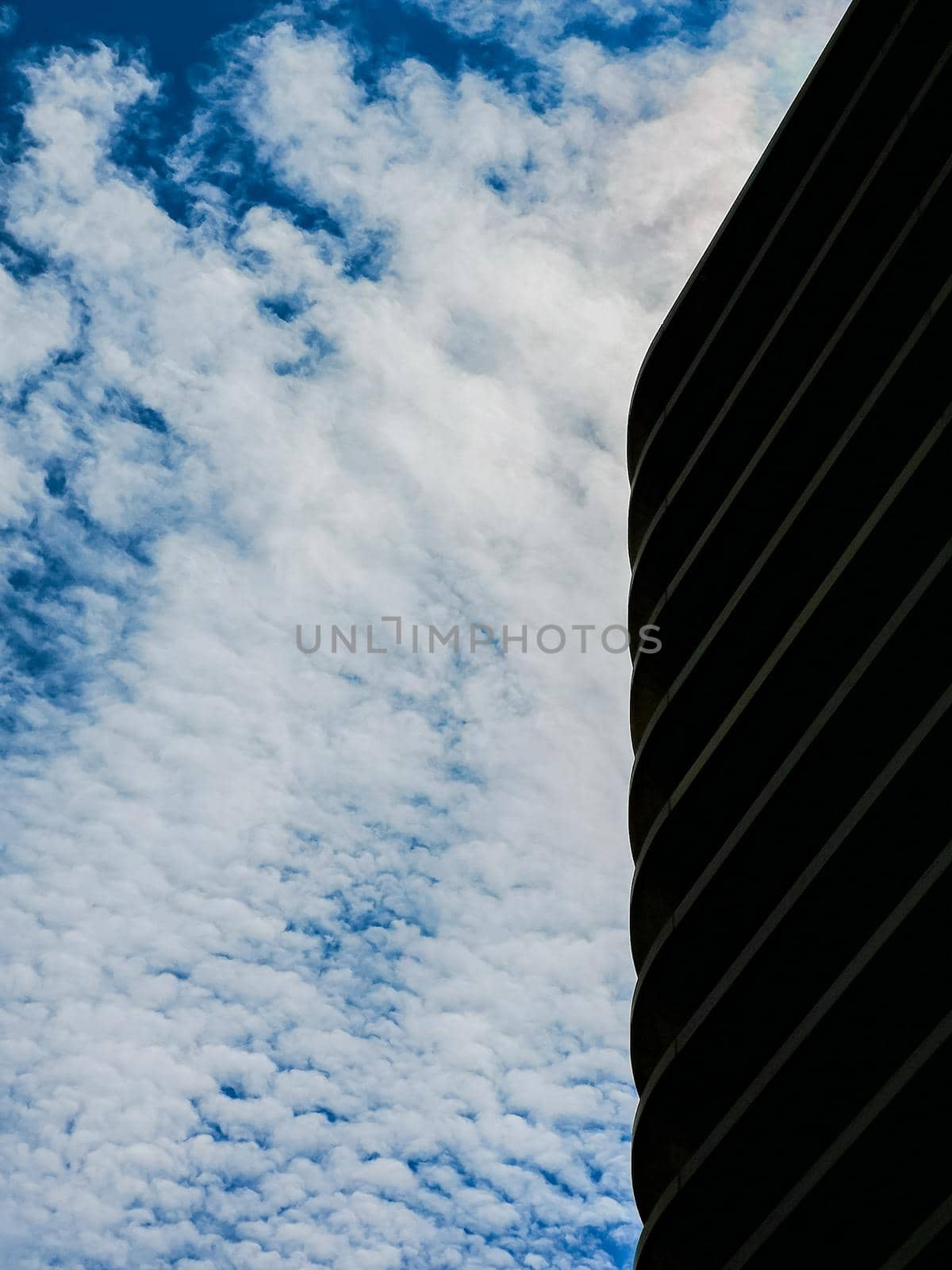 Looking up to wall of building in front of blue cloudy sky by Wierzchu