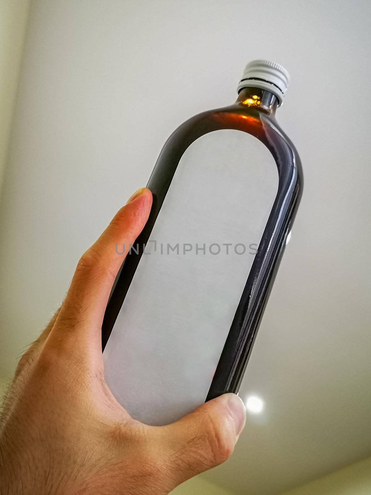 Wide high dark bottle with white label holded in hand by Wierzchu