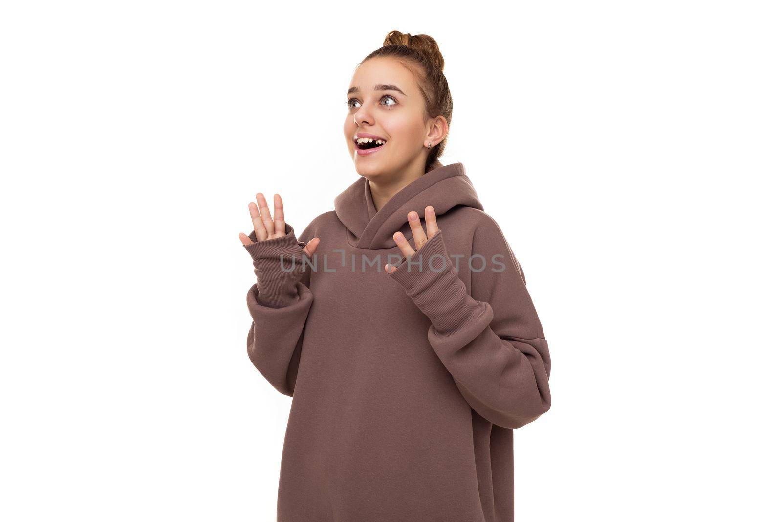 Photo of a beautiful cute girl with dark hair and a bun in a brown hoodie with a hood looks up in surprise isolated on a white background with free space for text.