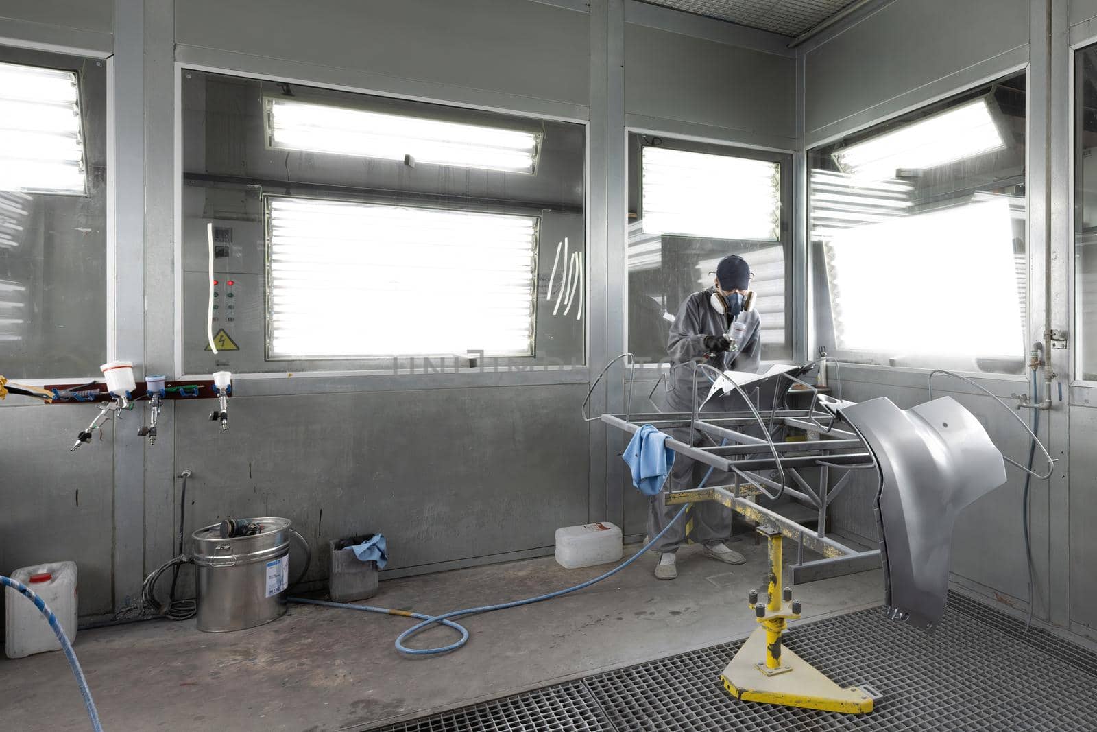 Automotive industry - engineer painting and working on a gray body of a car and wearing protective gear.