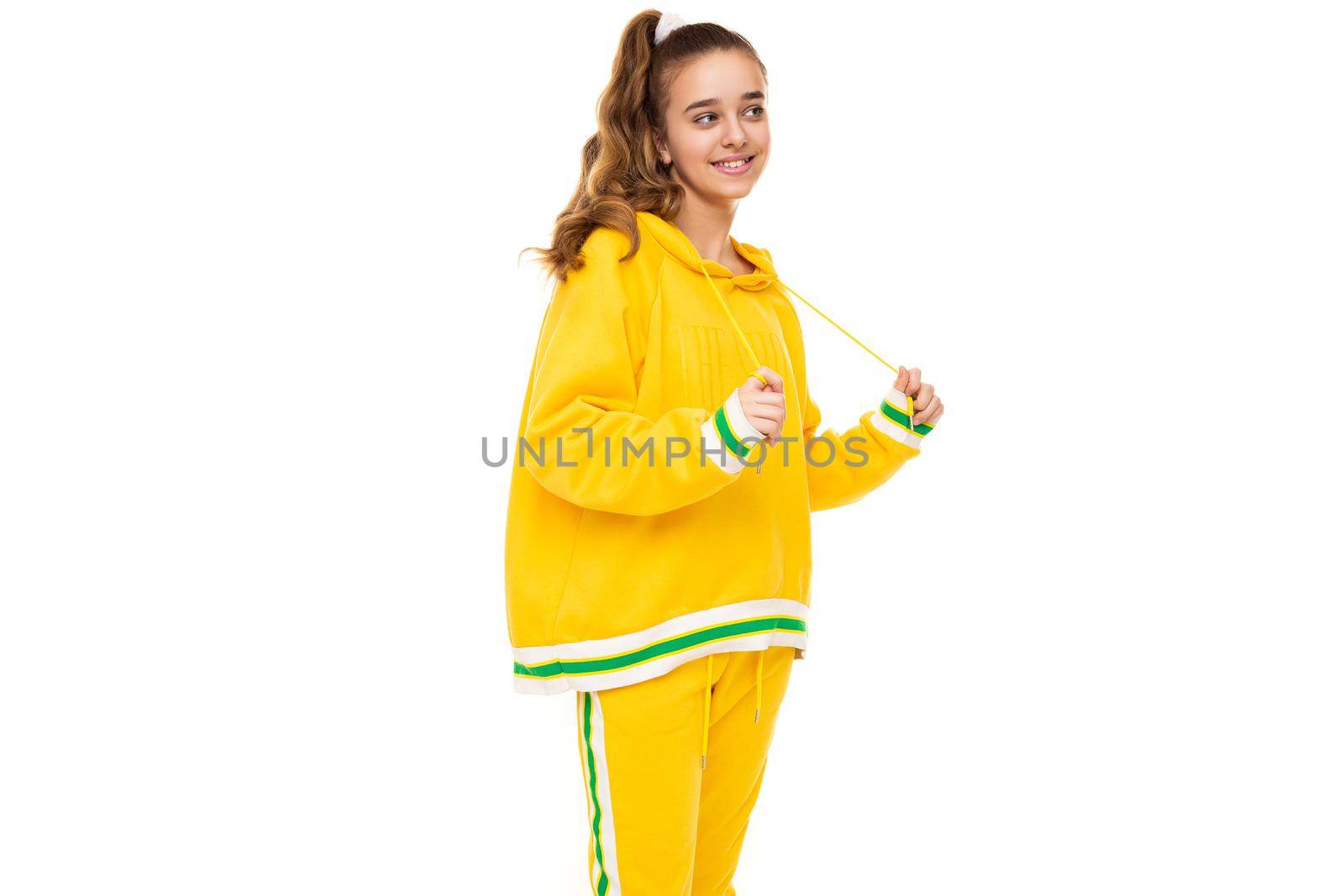 Photo of beautiful funny happy wonderful smiling cute girl with dark hair with ponytail in stylish yellow tracksuit with green stripes isolated on white background with free space for text.