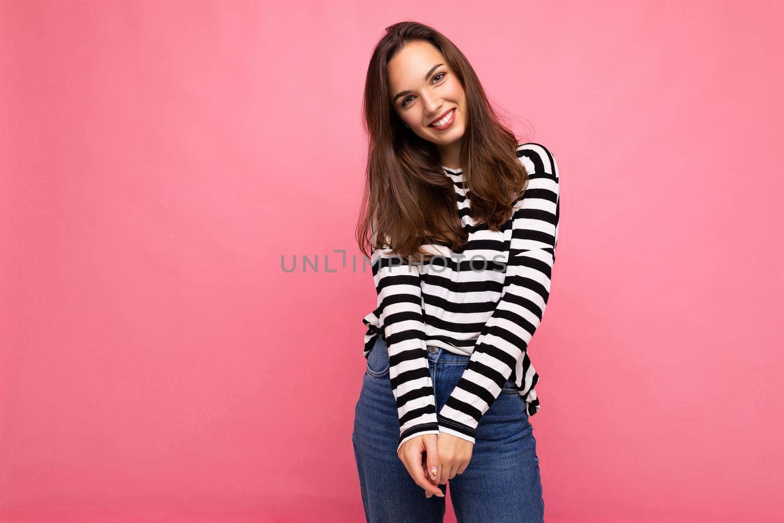 Photo of young european positive smiling winsome happy beautiful brunette woman with sincere emotions wearing casual striped pullover isolated on pink background with copy space for text.