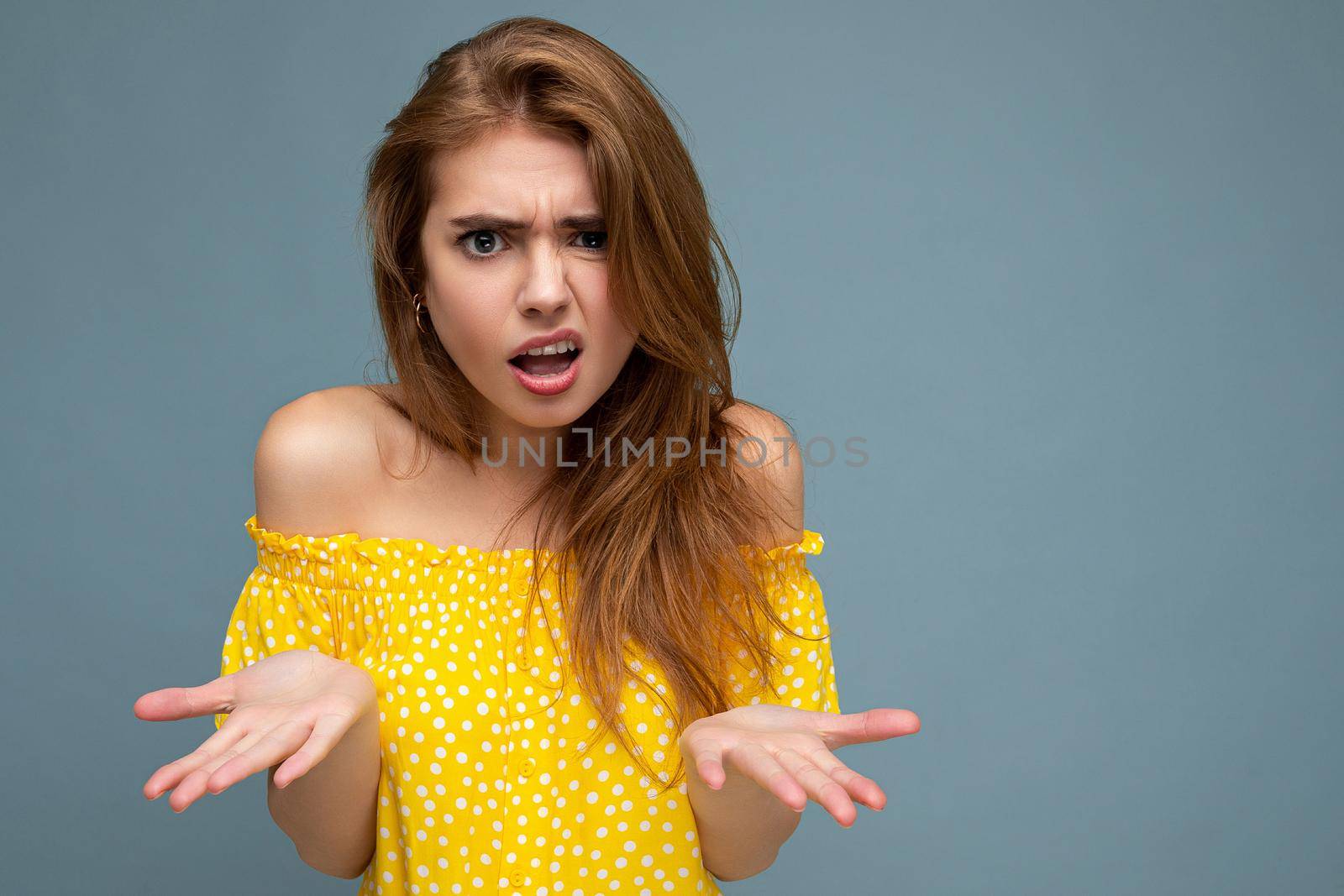 Photo of young cute delightful beautiful attractive angry asking dissatisfied unhappy dark blonde woman with sincere emotions isolated on blue background wall with copy space for text wearing stylish yellow dress.