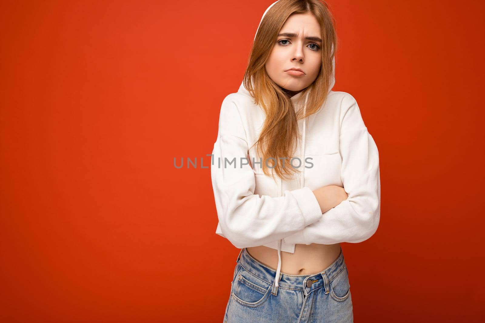 Dissatisfied angry young beautiful dark blonde female person with sincere emotions isolated on background wall with copy space for text wearing casual white hoodie. Negative concept.