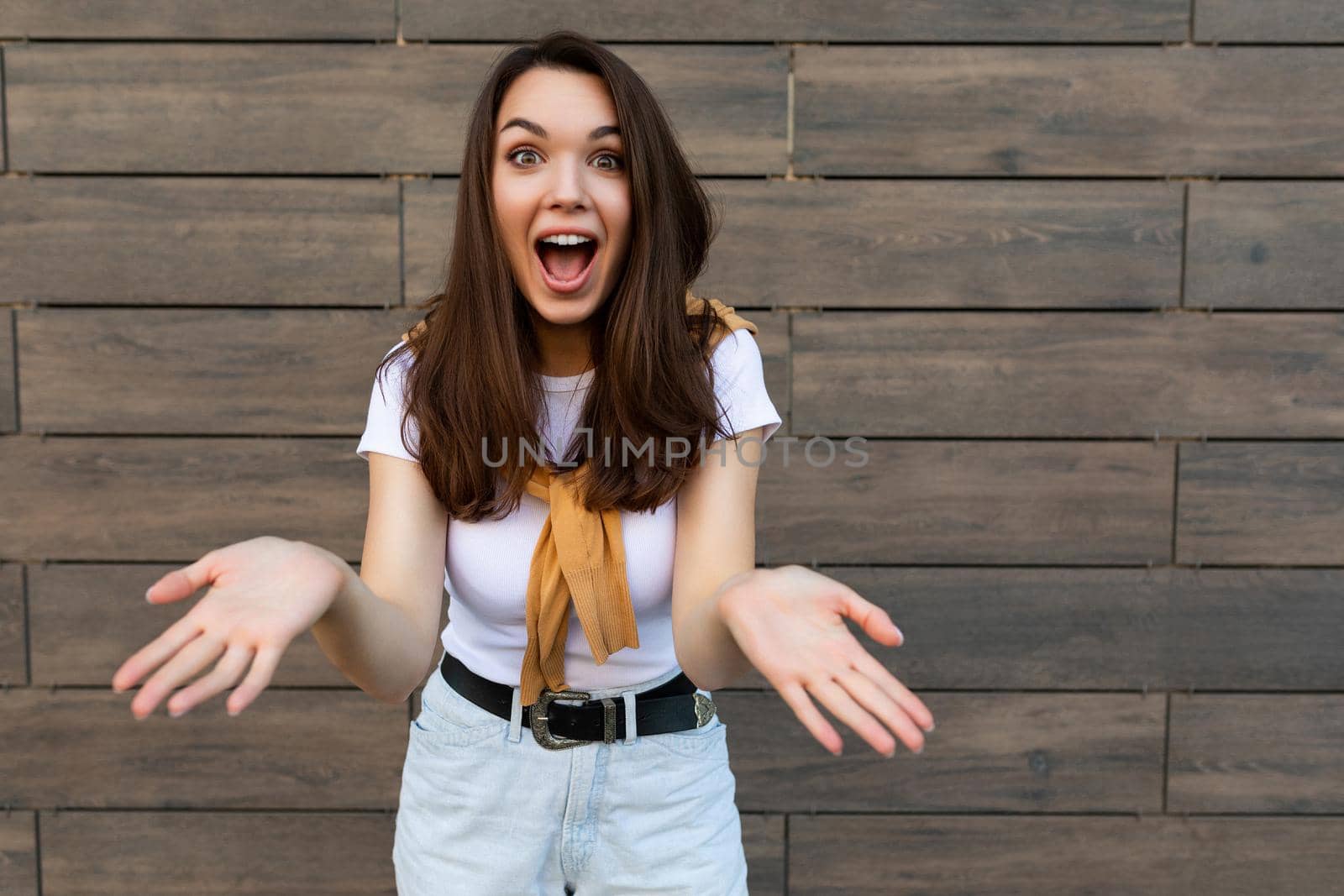 Close-up photo of pretty attractive beautiful happy positive charming amazed surprised shocked young brunette young woman wearing stylish clothes in the street near brown wall.