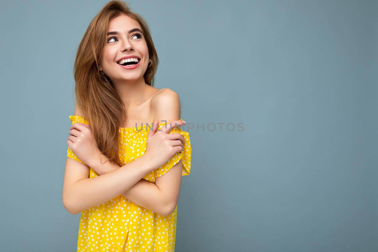 Photo of young cute delightful beautiful attractive smiling positive happy dark blonde woman with sincere emotions isolated on blue background wall with copy space for text wearing stylish yellow dress. Positive concept.
