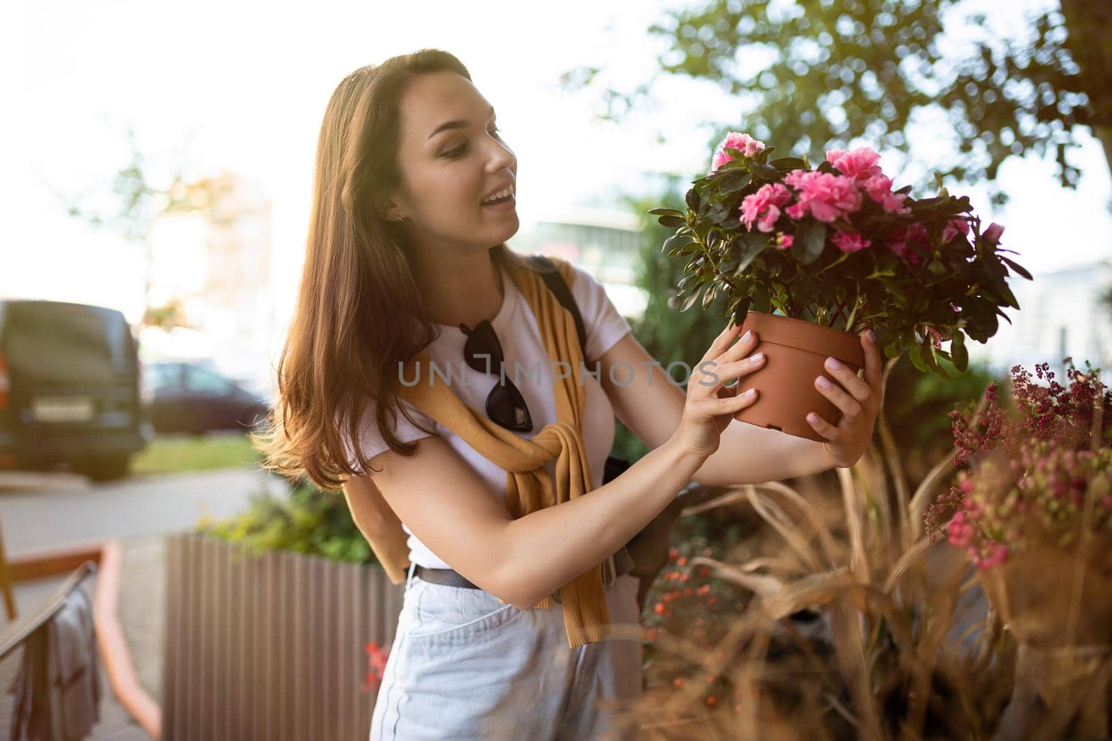 Photo of european beautiful attractive positive happy brunette woman wearing stylish white t-shirt and blue jeans chooses flowers as a gift in a street garden stall in the town.