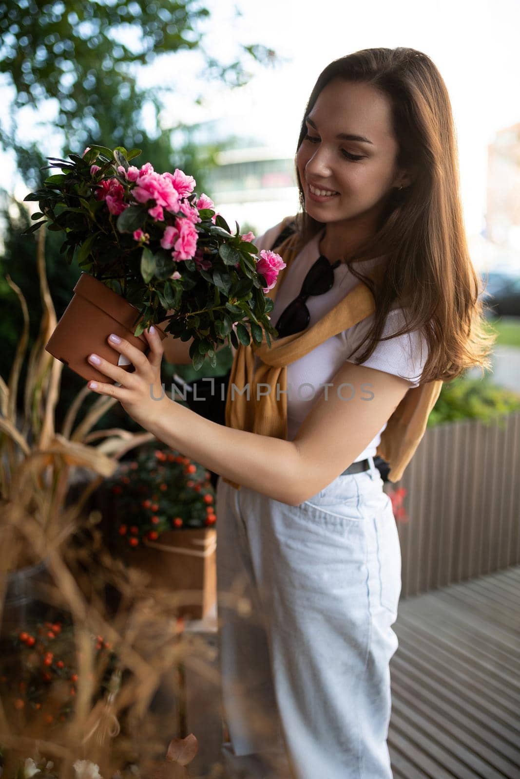 Vertical photo shot of european amazing beautiful attractive positive happy smiling young brunette woman in casual stylish look buys flowers in the store in the city.
