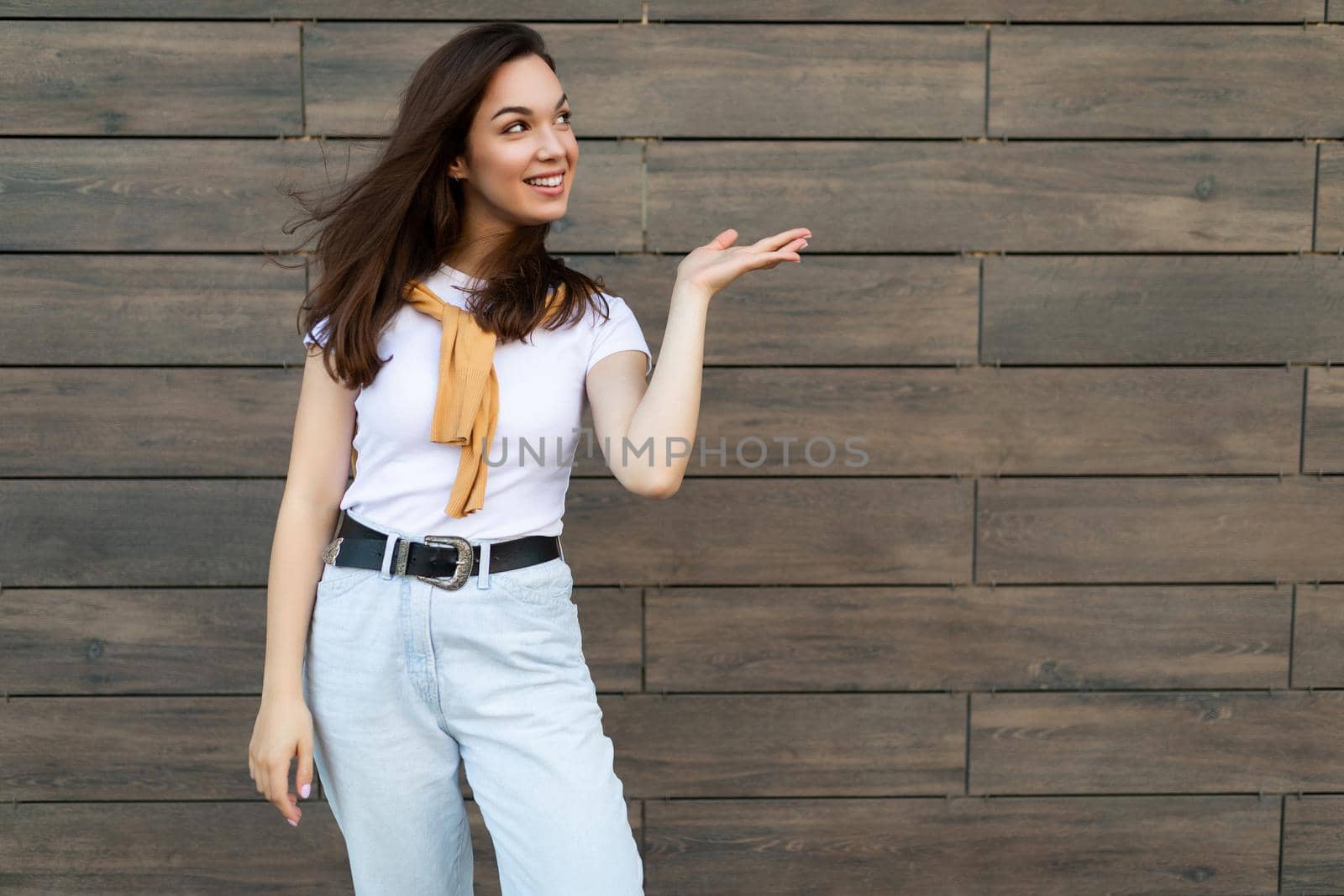 Close-up photo of pretty attractive beautiful smiling happy positive charming young brunette young woman wearing stylish clothes in the street near brown wall with copy space for text.