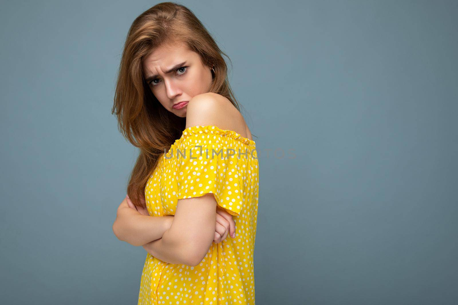 Photo of young cute delightful beautiful attractive sad dissatisfied unhappy dark blonde woman with sincere emotions isolated on blue background wall with copy space for text wearing stylish yellow dress.