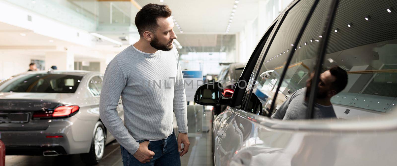 young man chooses a new car in a premium car dealership.