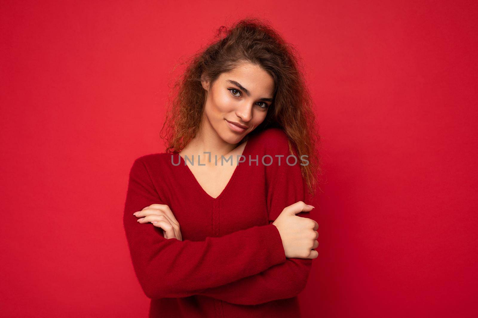 Adult shy beautiful self-confident curly brunette woman with sincere emotions poising isolated on background wall with copy space wearing casual dark red sweater. Positive concept.