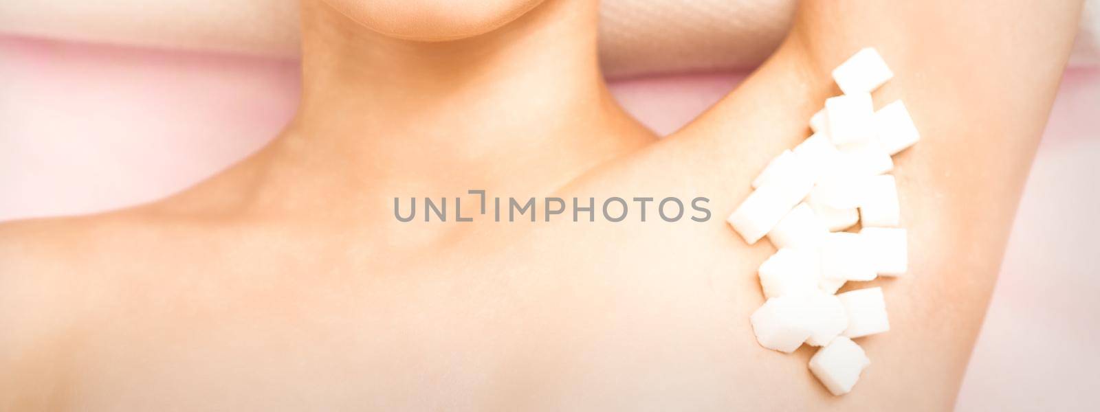 Sugaring, waxing concept. White sugar cubes lie down on the female armpit of the young white woman, close up