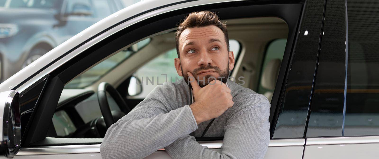 A man sits inside a car thinking about buying on credit at a car dealership.