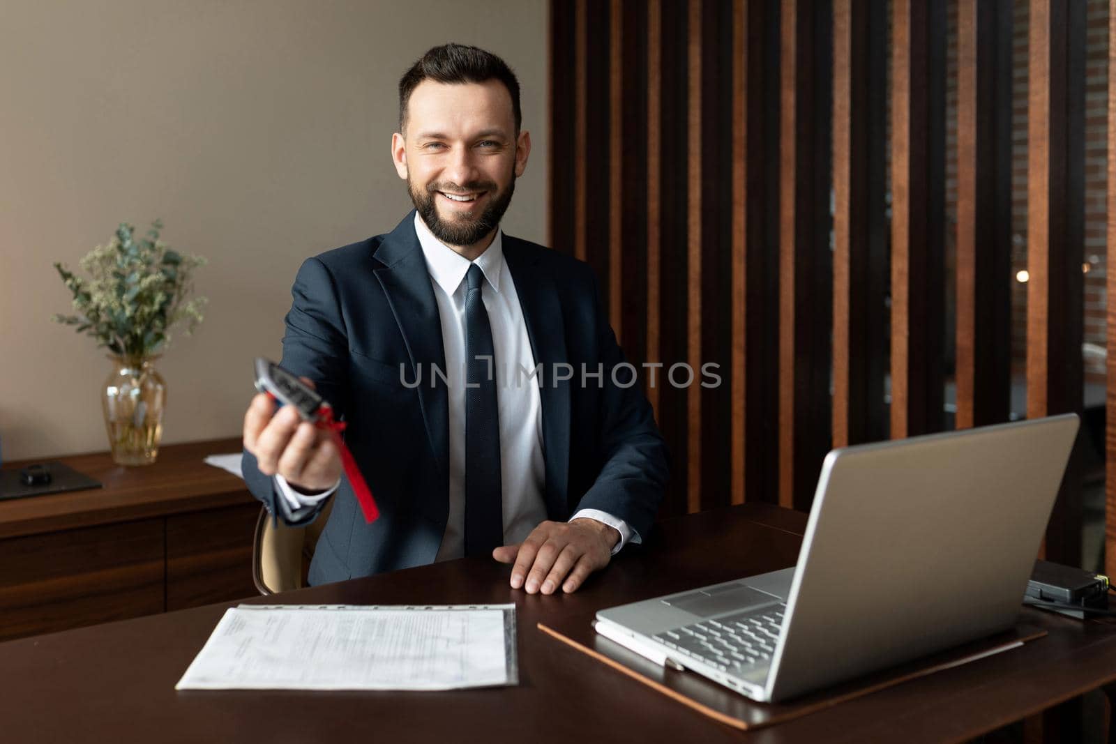 car dealership manager holding out keys to a new car after making a successful deal.