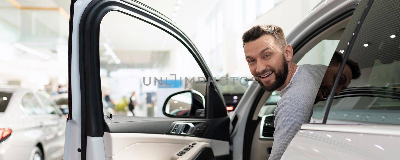 satisfied customer peeks out from behind the wheel of a new SUV at a car dealership.