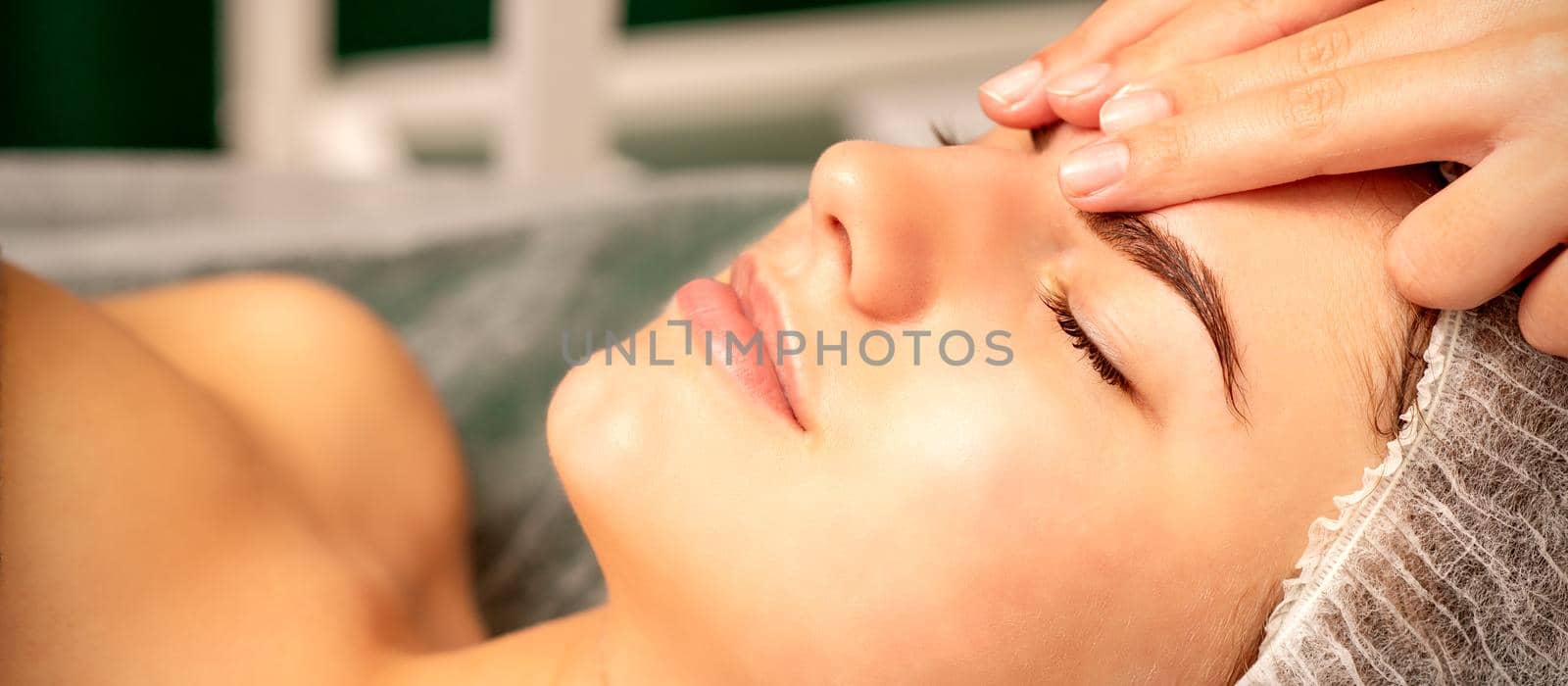 Head massage. Beautiful caucasian young white woman receiving a head and forehead massage with closed eyes in a spa salon. by okskukuruza