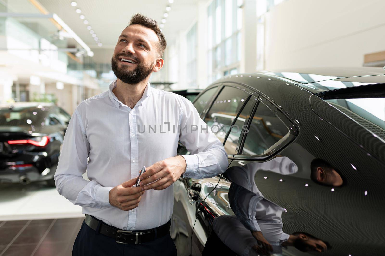a man in a car dealership dreaming about a new car with a smile on his face.