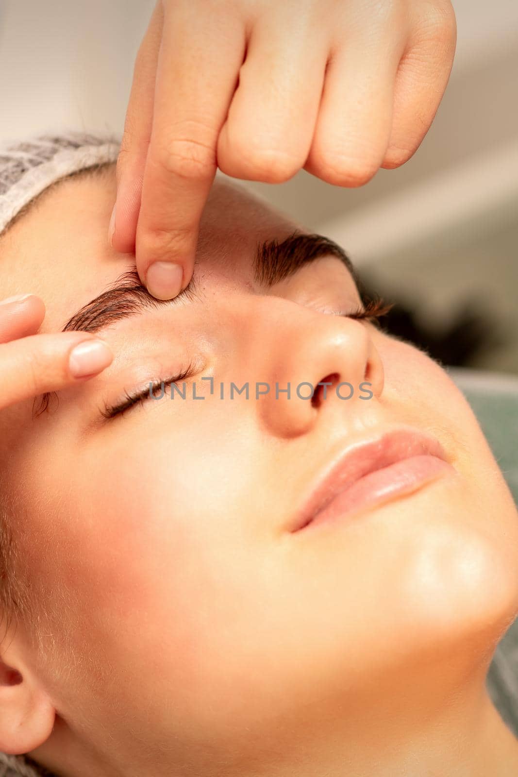 Eyebrow massage. Beautiful caucasian young white woman receiving an eye and eyebrow massage with closed eyes in a spa salon. by okskukuruza