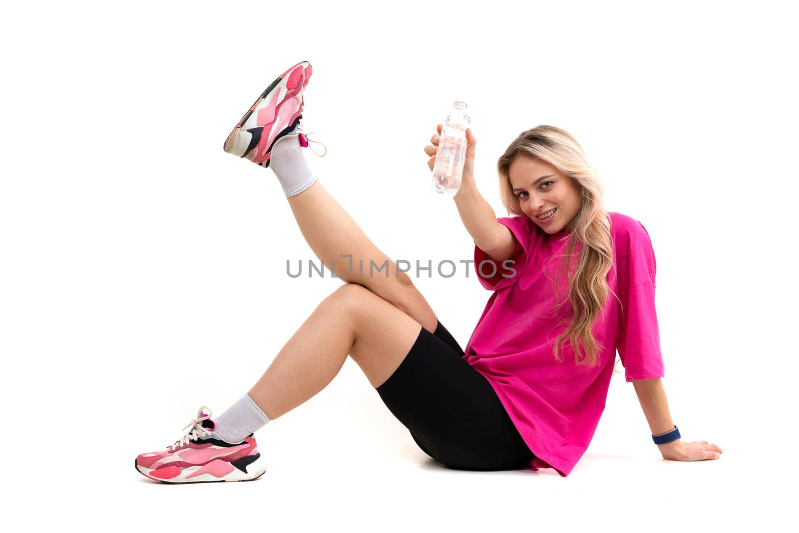 sports blonde sits on a white background with a bottle in her hands in sneakers.