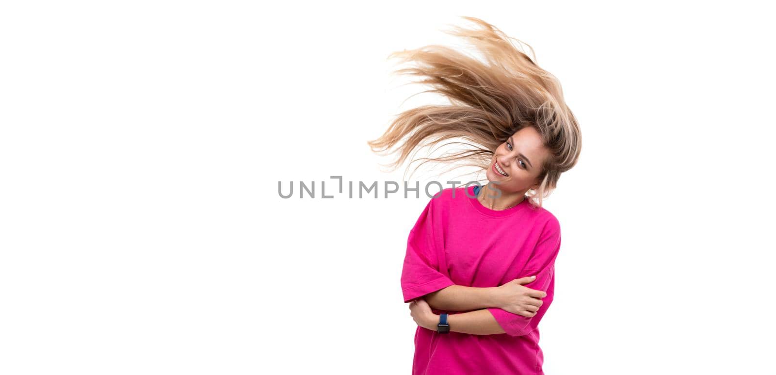 portrait of a cheerful young woman in a fuchsia t-shirt with hair flying in the wind on a white background.