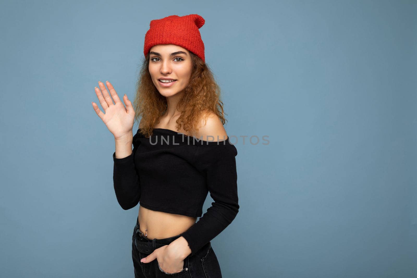 Photo of young positive happy smiling beautiful woman with sincere emotions wearing stylish clothes isolated over background with copy space and waving with hand. Hello concept by TRMK