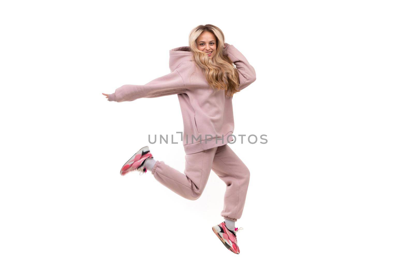 young woman in a jump on a white background in a pink sports suit.