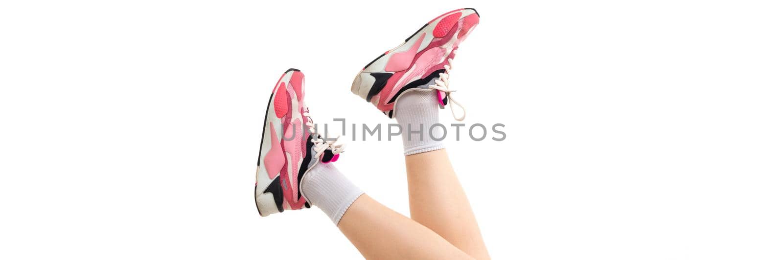 photo of female legs in pink sneakers on a white background.