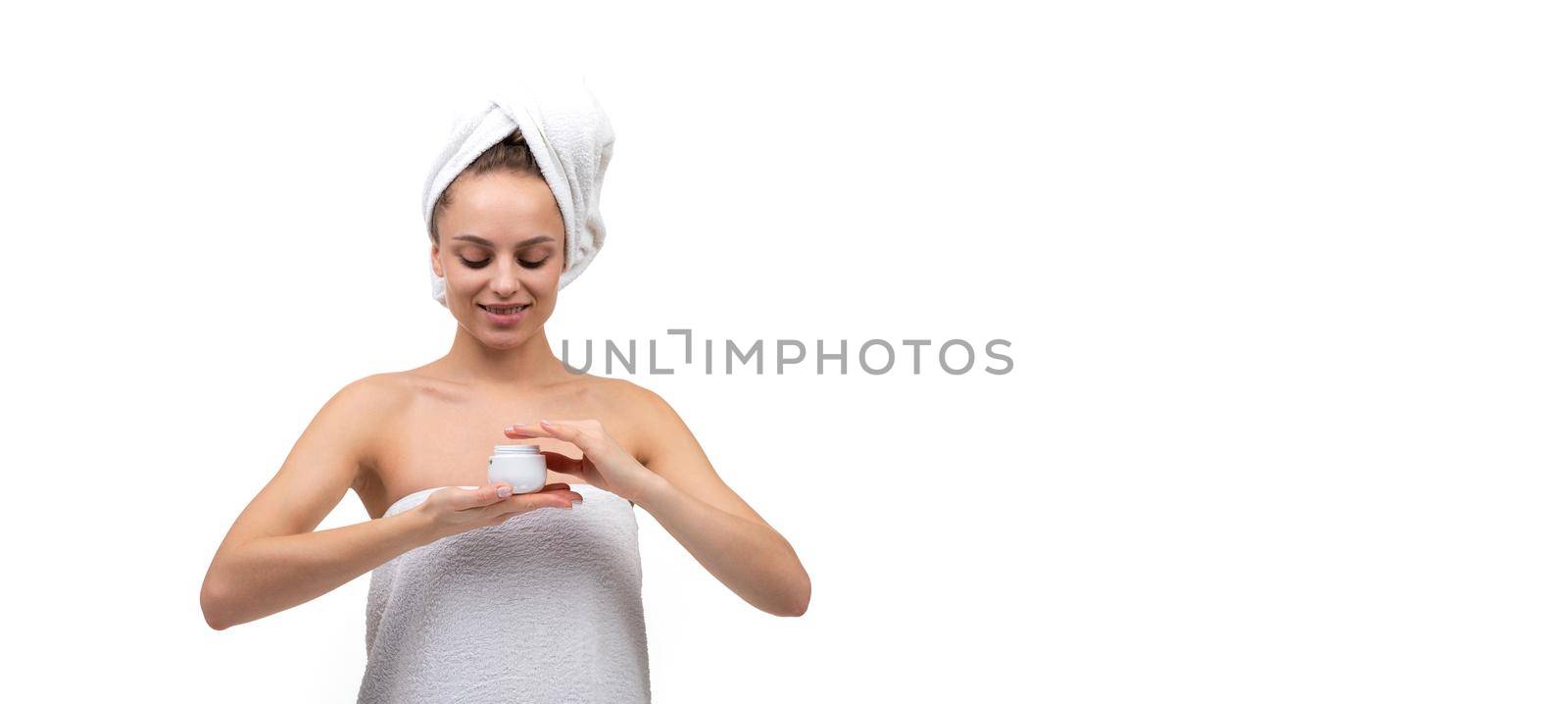 young woman after a shower on a white background with a jar of white cream in her hands.