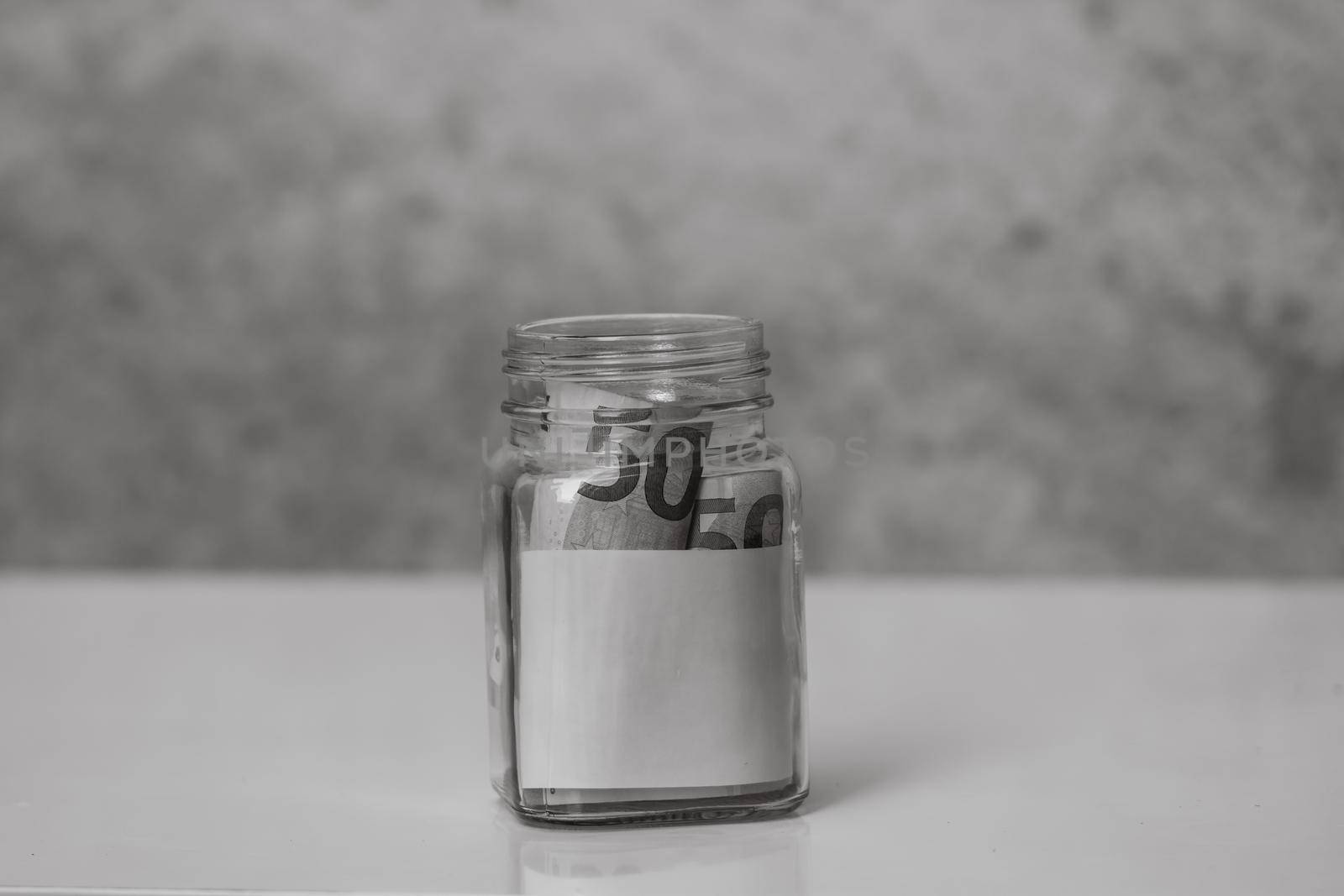 Composition with saving money banknotes (50 EURO) in a glass jar with empty white label or note for your text. Concept of investing and keeping money, close up isolated.
