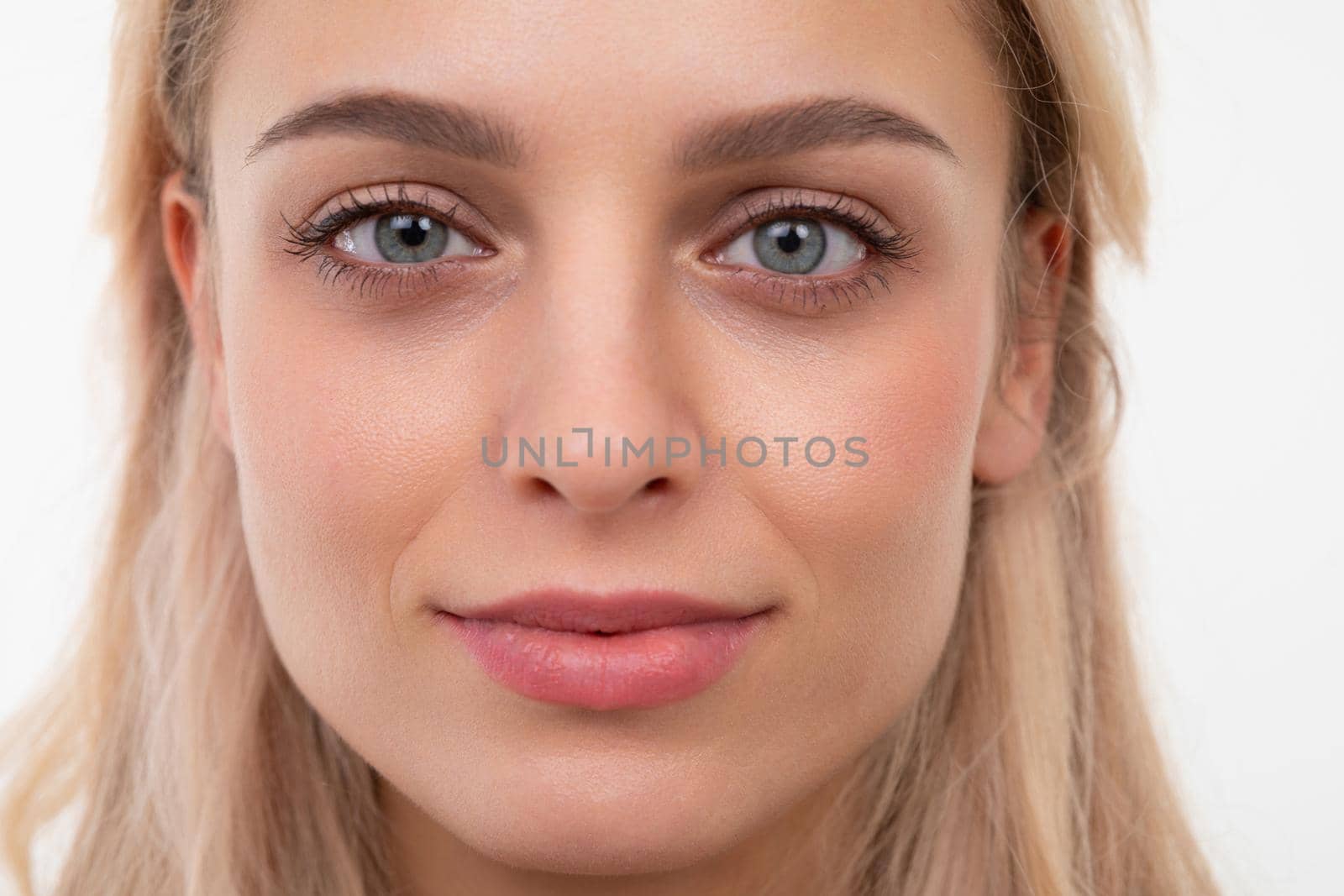 close-up portrait of a blonde of European appearance on a white background looking at the camera with a slight smile on her face.
