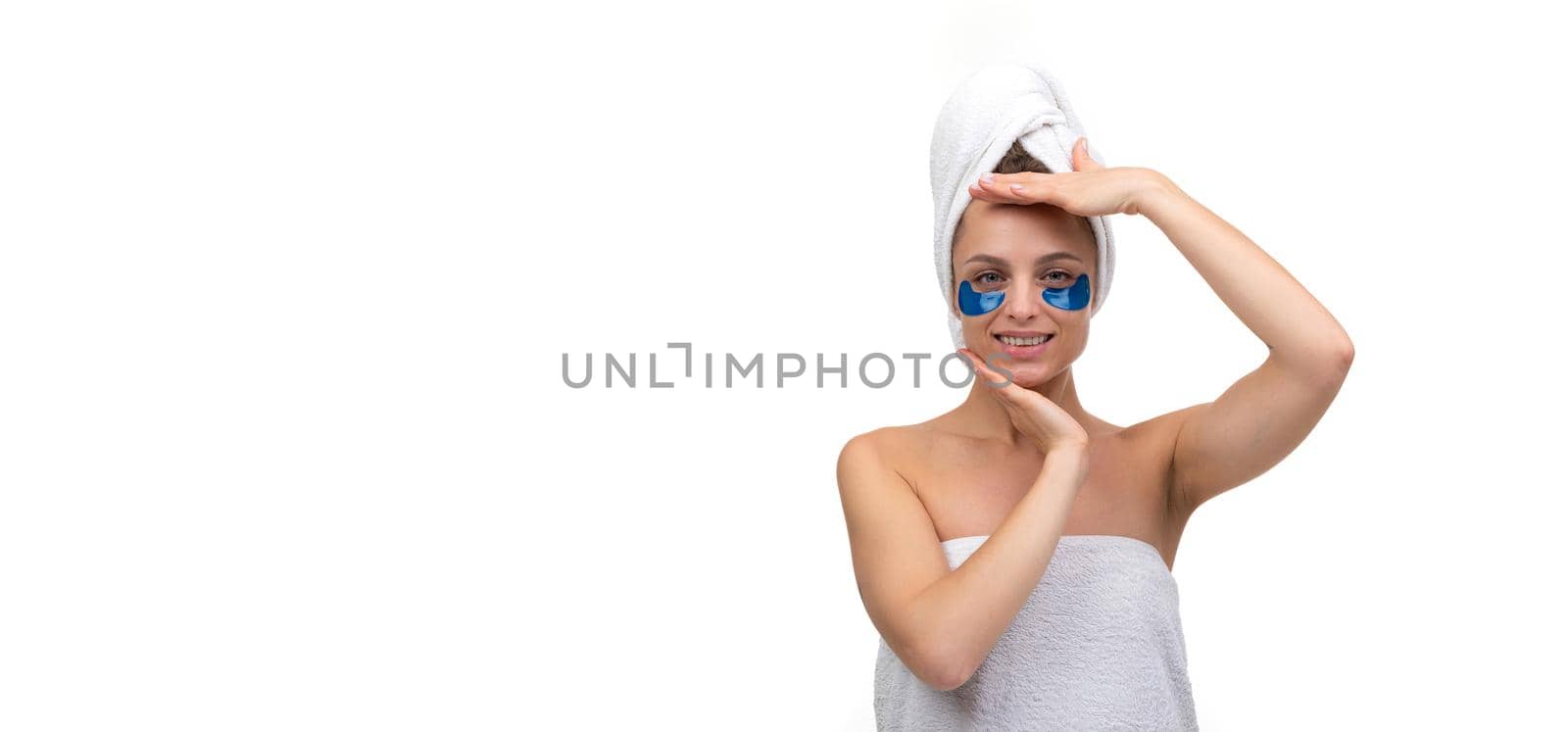 young woman after spa treatments in a towel on her body and cosmetic patches on her face looks at the camera.