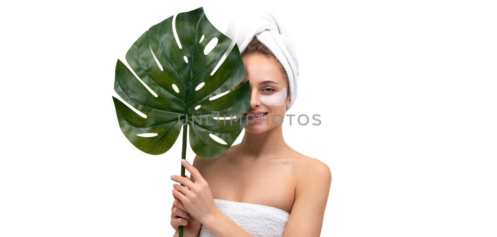 portrait of a young woman with well-groomed skin after a shower on a white background with a palm leaf in her hands.